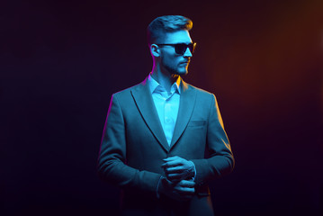 Young handsome model posing in a studio in a trendy neon light. Fashionable man in a stylish suit....