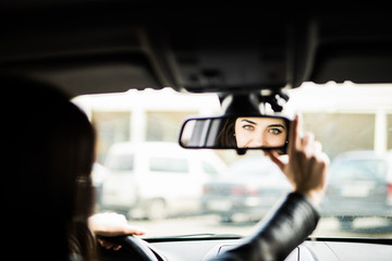 Rear view of attractive young woman in casual wear looking in rear-view mirror and smiling while driving a car - Powered by Adobe