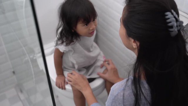 asian woman help her daughter to sit on the toilet while peeing