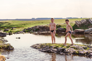 two cheerful boys in bathing shorts play on a small river in the village
