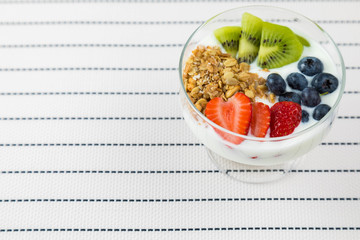 Bowl of homemade granola with yogurt and fresh berries: strawberry, kiwi and blueberry on white  background with strips from side view