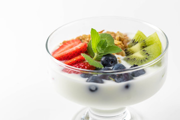 Bowl of homemade granola with yogurt and fresh berries: strawberry, kiwi and blueberry on white  background  from side view