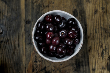 fresh organic ripe black cherries in a white bowl on a rustic wooden table