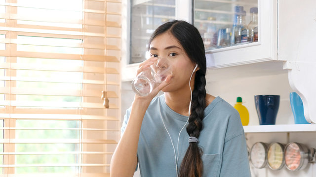 Young beautiful asian woman drinking water while standing by window in kitchen background, people and healthy lifestyles
