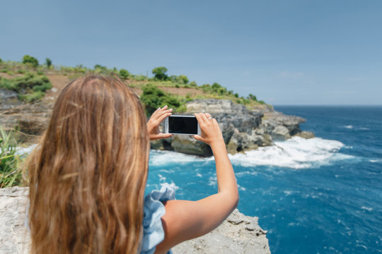 Tourist taking picture on her smartphone from sea cliff. Young girl photograph  on smart phone gadget, blogger using in female hand mobile screen on background seascape,  lifestyle concept