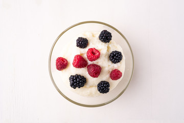 Semolina pudding porridge dessert with  blackberry and raspberry berries in glass bowl, breakfast, white wooden background, isolated