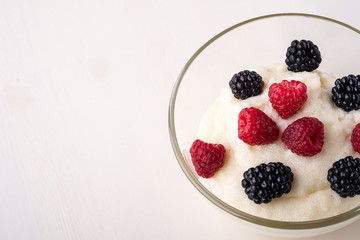 Semolina pudding porridge dessert with  blackberry and raspberry berries in glass bowl, breakfast, white wooden background, isolated
