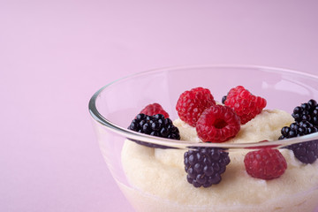 Semolina pudding porridge dessert with  blackberry and raspberry berries in glass bowl, breakfast, pink background, isolated