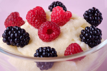 Semolina pudding porridge dessert with  blackberry and raspberry berries in glass bowl, breakfast, pink background, isolated