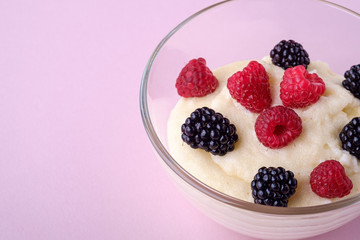 Semolina pudding porridge dessert with  blackberry and raspberry berries in glass bowl, breakfast, pink background, isolated