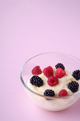 Semolina pudding porridge dessert with  blackberry and raspberry berries in glass bowl, breakfast, pink background, isolated