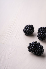 Three blackberry berries macro close up on white wooden background isolated copy space