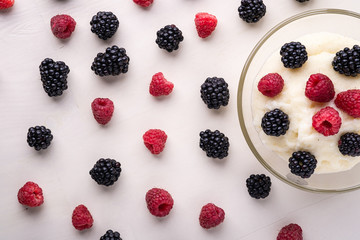 Semolina pudding porridge dessert with  blackberry and raspberry in glass bowl near with scattered heap in order berries on white wooden background, breakfast, isolated, top view