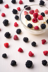 Semolina pudding porridge dessert with  blackberry and raspberry in glass bowl near with scattered heap in order berries on white wooden background, breakfast, isolated, selective focus