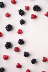Blackberry and raspberry scattered heap in order berries on white wooden background copy space, isolated, texture