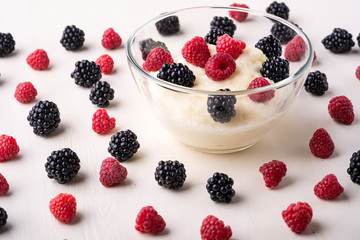 Semolina pudding porridge dessert with  blackberry and raspberry in glass bowl near with scattered heap in order berries on white wooden background, breakfast, isolated, selective focus