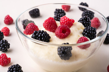 Semolina pudding porridge dessert with  blackberry and raspberry in glass bowl near with scattered heap in order berries on white wooden background, breakfast, isolated, selective focus
