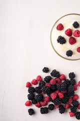 Semolina pudding porridge dessert with  blackberry and raspberry in glass bowl near with scattered heap berries on white wooden background, breakfast, isolated, top view