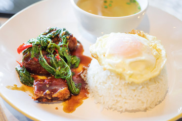 Stir fried spicy crispy pork with basil with rice and sunny-side-up fried egg on top. 