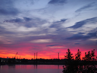 Beautiful red and yellow sunset over the city is reflected in the river water with silhouette of a city road on the background. Panoramic landscape on the dusk.
