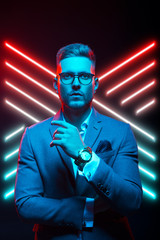 Young handsome model posing in a studio in a trendy neon light. Fashionable man in a stylish suit. Vibrant color. Bright colorful light effects. Disco style. Overlay. Gel filter. Supersaturated