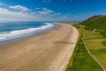Aerial view of the huge sandy beach and green hills in Rhossili, Swansea
