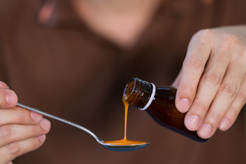 Man hand pouring medication or antipyretic syrup from bottle to spoon
