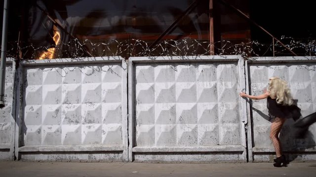 Young strange woman in black dress and stockings walks and moves along white fence with barbed wire. Video concept restriction of freedoms in Russia