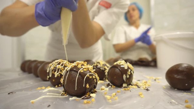Decorating and making chocolate round cakes from kako. Women make cakes at a confectionery factory. Decorating sweets with cream and nuts, food industry