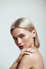 Perfection. Vertical photo of sexy young woman with blond hair and perfect shiny skin looking at camera while standing against grey background - obrazy, fototapety, plakaty
