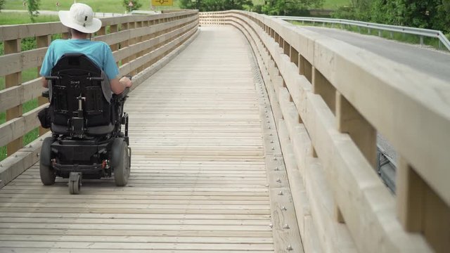 4k resolution video of a man on electrical wheelchair driving on wooden bridge