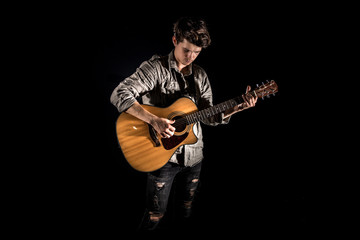 Guitarist, music. A young man plays an acoustic guitar on a black isolated background