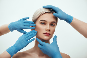 Facial surgery. Beautiful blonde woman waiting for facial surgery while surgeons in blue medical...