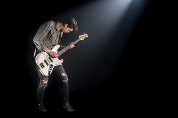 the musician plays bass guitar, on a black background with a beam of light
