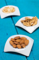Food,taste and snack concept: almonds nuts in a porcelain small saucer on a blue wooden background.