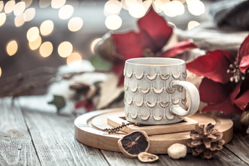 Coffee cup over Christmas lights bokeh in home on wooden table with flowers on a background and decorations. Holiday decoration, magic Christmas