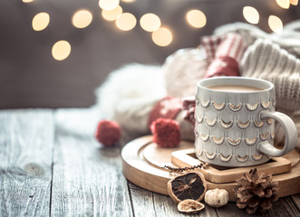 Coffee cup over Christmas lights bokeh in home on wooden table with sweater on a background and decorations. Holiday decoration, magic Christmas