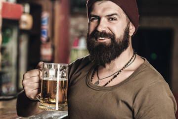 Happy handsome young man drinks beer at the bar counter. Bearded hipster drinking beer. Beer pub....