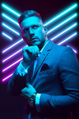 Young handsome model posing in a studio in a trendy neon light. Fashionable man in a stylish suit. Vibrant color. Bright colorful light effects. Disco style. Overlay. Gel filter. Supersaturated