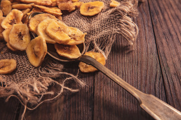 Dried bananas stacked on a fabric and spoon over old brown table. Composition in the old style