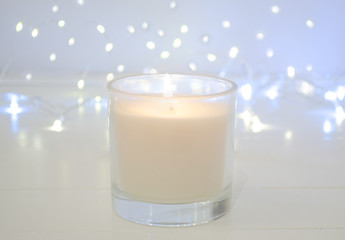 White candle on white background with bokeh lights. Christmas concept. Copy space. Simple minimalism concept. Candle flame at night with bokeh. Abstract blurred background. .