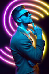 Young handsome model posing in a studio in a trendy neon light. Fashionable man in a stylish suit. Vibrant color. Bright colorful light effects. Disco style. Overlay. Gel filter. Supersaturated