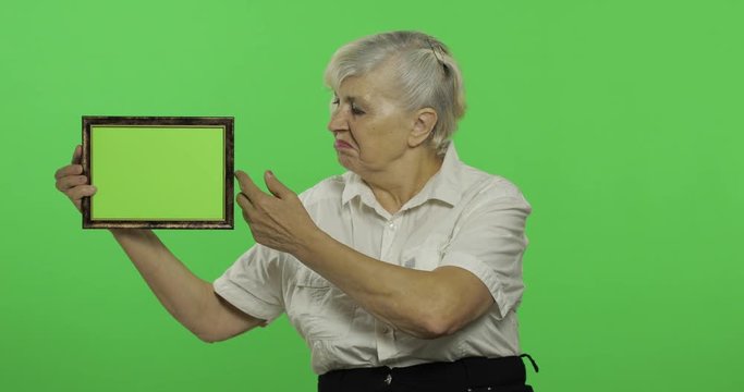 An elderly woman holding a frame with green image. Old grandmother. Chroma key