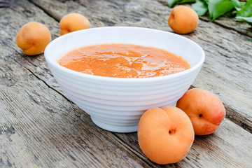 Apricot jam in a white bowl and ripe apricots on a wooden table.