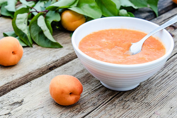 Apricot jam in a white bowl and ripe apricots on a wooden table.