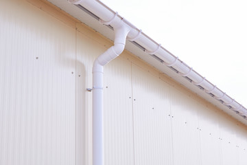 White plastic rain guttering system. Guttering drainage pipe exterior. Background of sandwich panel 