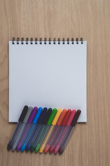 Obraz premium Notepad or notebook with Many colorful pens on brown wood table.using for education, business background