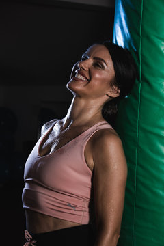 Young female boxer pose near bag on a sports training in a gym.