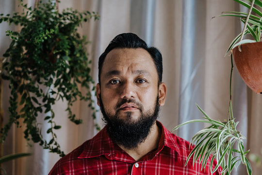 Portrait Of Asian Handsome Middle Age Man With A Mustache And Beard With Flower Plants In The Background.