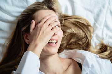 Fototapeta premium Portrait beautiful blonde woman with a beautiful face and amazing eyes, lies, sleeps on the bed linen in an elegant. And sensual looks and flirtatious smile. Health and harmony concept